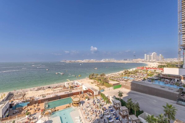 A hotel with a pool area, beach access, and a view of the ocean and city skyline.