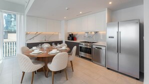 Een moderne keuken met witte kasten, roestvrijstalen apparatuur en een eethoek met een houten tafel en witte stoelen.