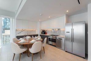 Une cuisine moderne avec des meubles blancs, des appareils en acier inoxydable et un coin repas comprenant une table en bois et des chaises blanches.