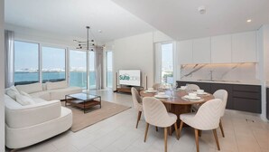 A modern living room with a sofa, dining table, and chairs. There is a television on the wall and a view of the sea through large windows. - Beautiful 2 Bedroom Sea Views at La Vie JBR (Dubai)