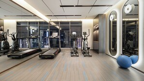 Une salle de sport moderne équipée de tapis de course, de vélos elliptiques et de ballons d’exercice, avec de grandes fenêtres offrant une vue sur la ville.