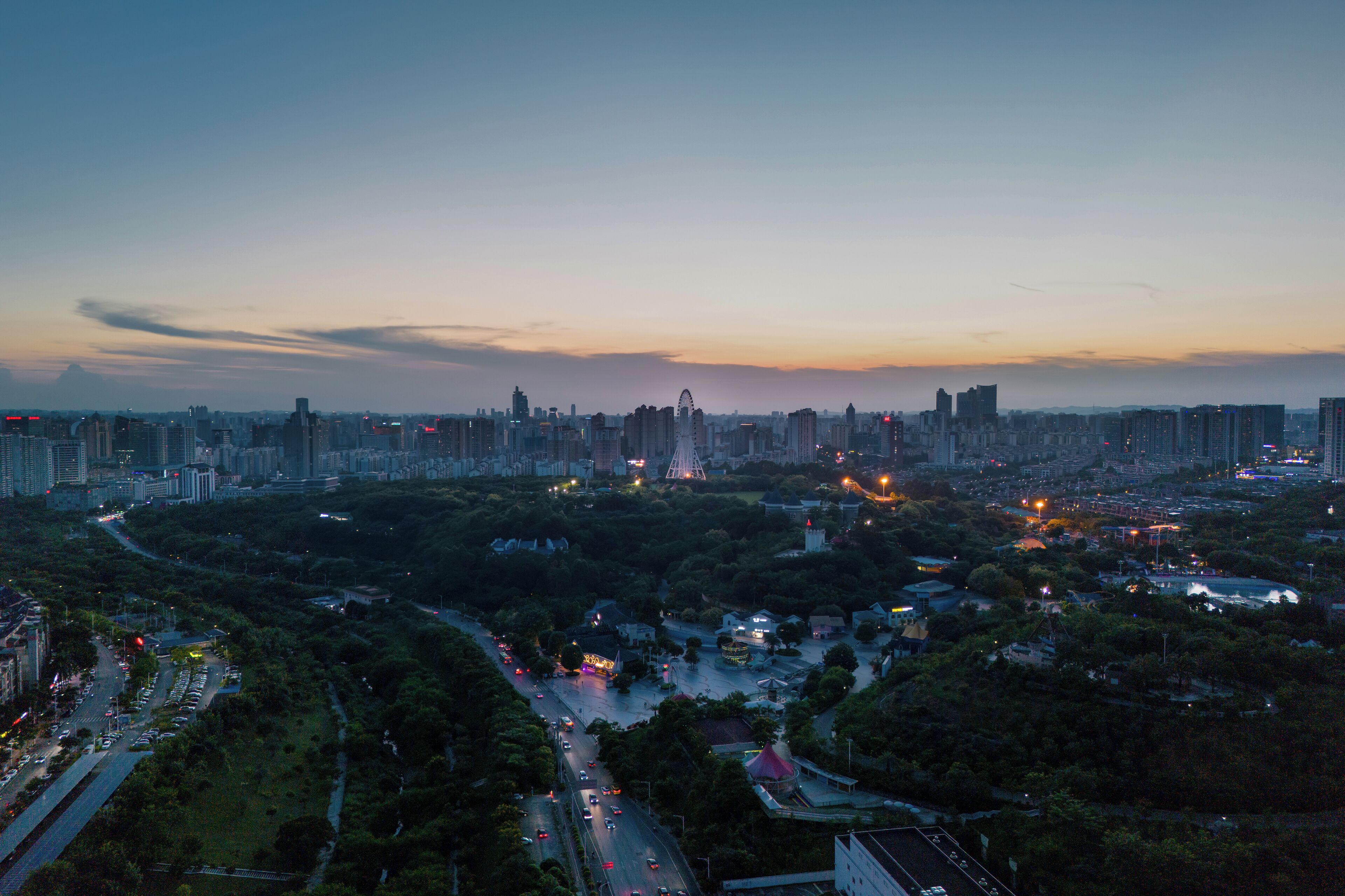 Un paisaje urbano al atardecer con rascacielos, una carretera serpenteante y una zona verde.