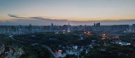 A cityscape at dusk with high-rise buildings, a winding road, and a park area.