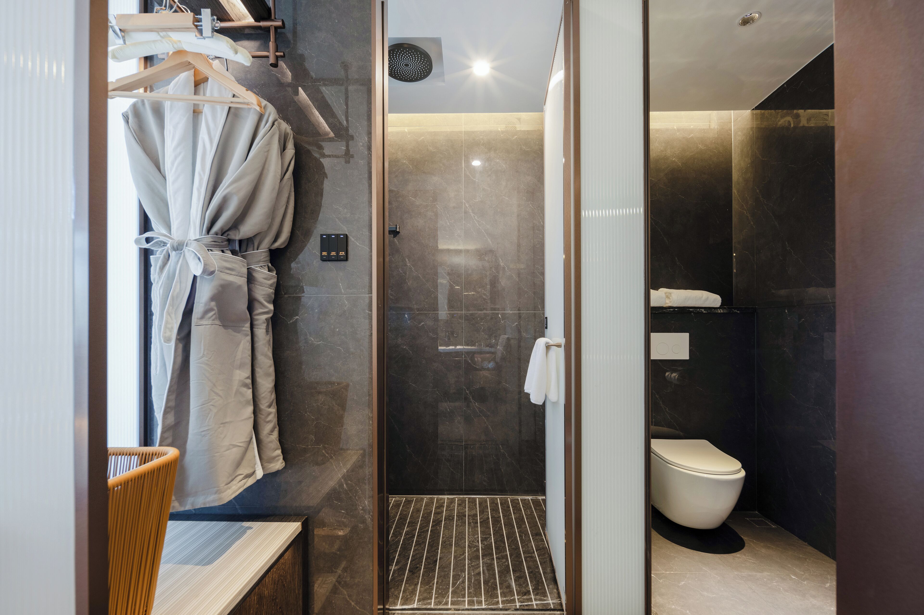 Un baño moderno con ducha de vidrio, inodoro blanco y una bata colgada en un perchero.