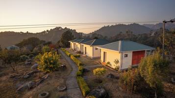 Stroll through a serene residential area with single-story houses along a paved pathway, surrounded by neatly trimmed hedges and rolling hills.