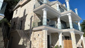 A two-story house with stone exterior, a balcony, and a garage. - Meliana Homes (Parga)