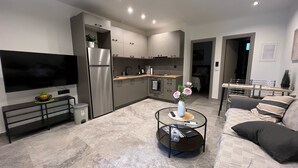 A modern kitchen with a built-in oven and refrigerator, a dining area with a table and chairs, and a living room with a sofa and a coffee table. - Meliana Homes (Parga)