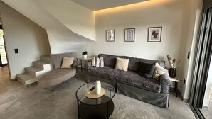A modern living room with a sofa, a coffee table, and a staircase. - Meliana Homes (Parga)