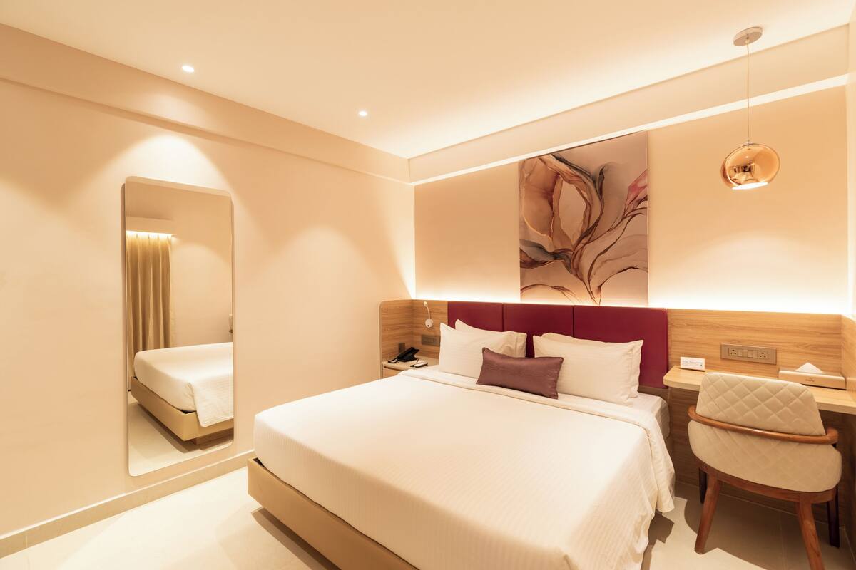 Quarto de hotel moderno com uma cama grande, mesa de cabeceira, cadeira e espelho.