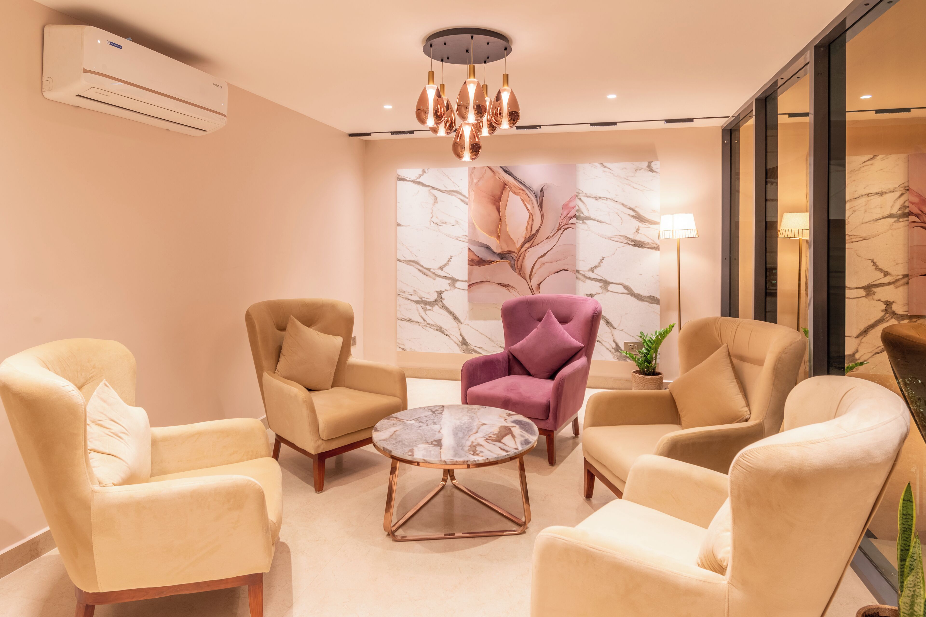 A modern living room with beige armchairs, a round coffee table, and a chandelier.