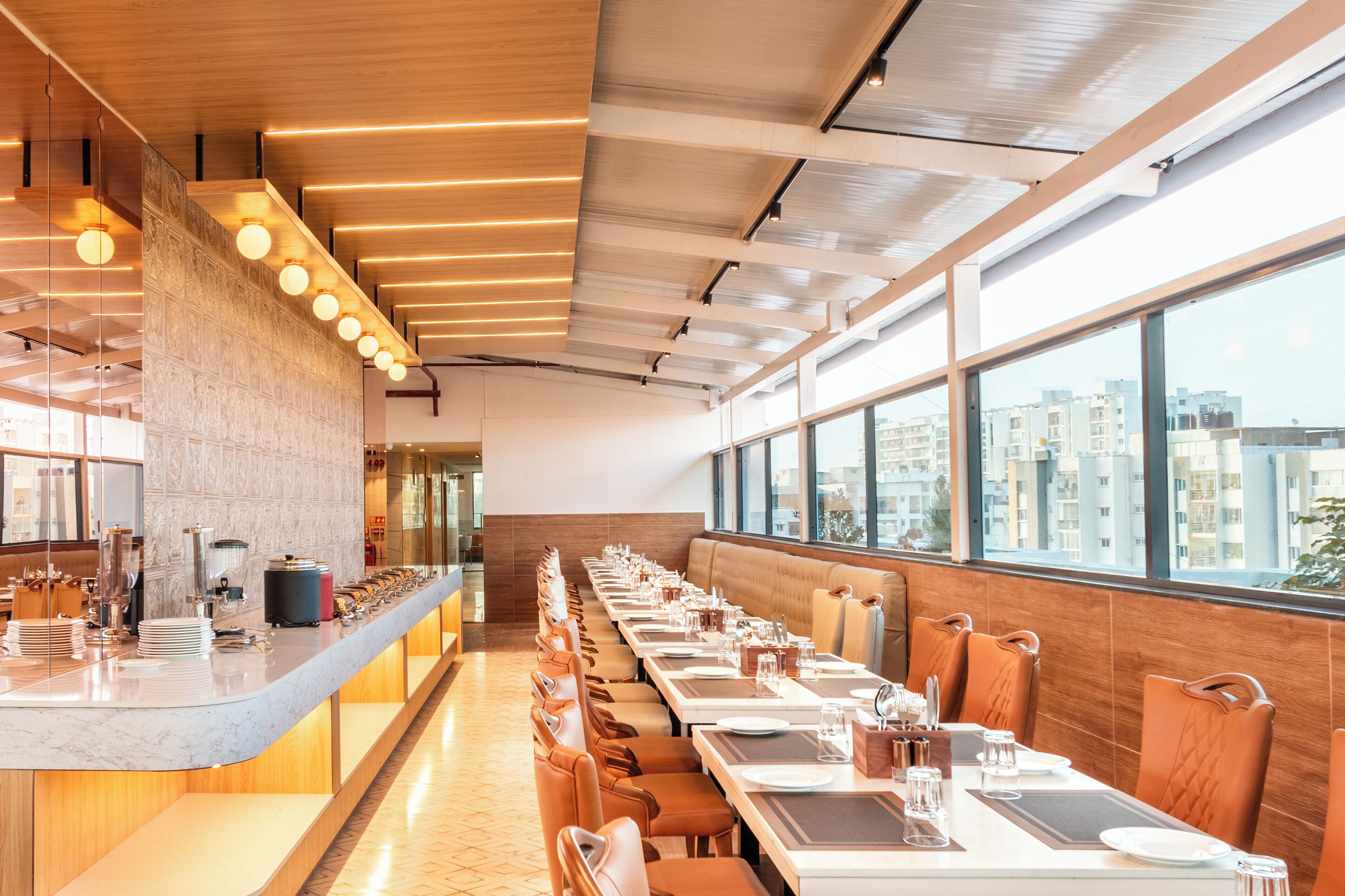 Un restaurant moderne doté d’un long comptoir, de nombreuses tables et offrant une vue sur les bâtiments grâce à de grandes fenêtres.