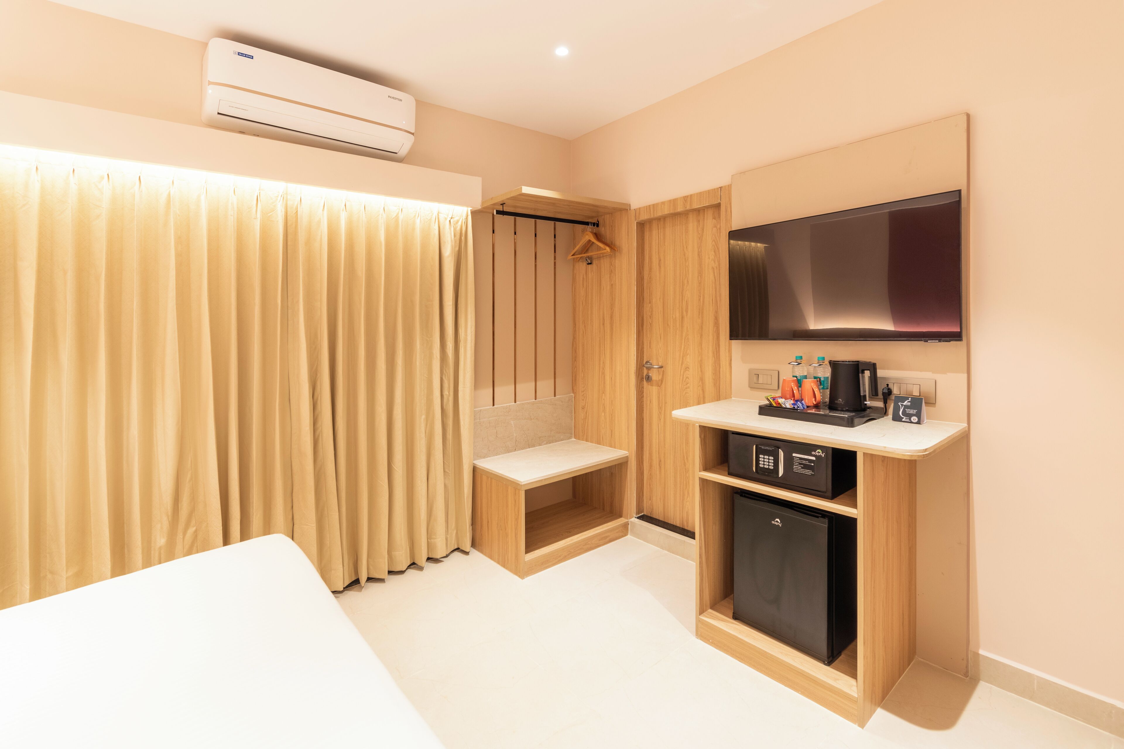 A hotel room with a bed, a TV, a minibar, and a shower area.