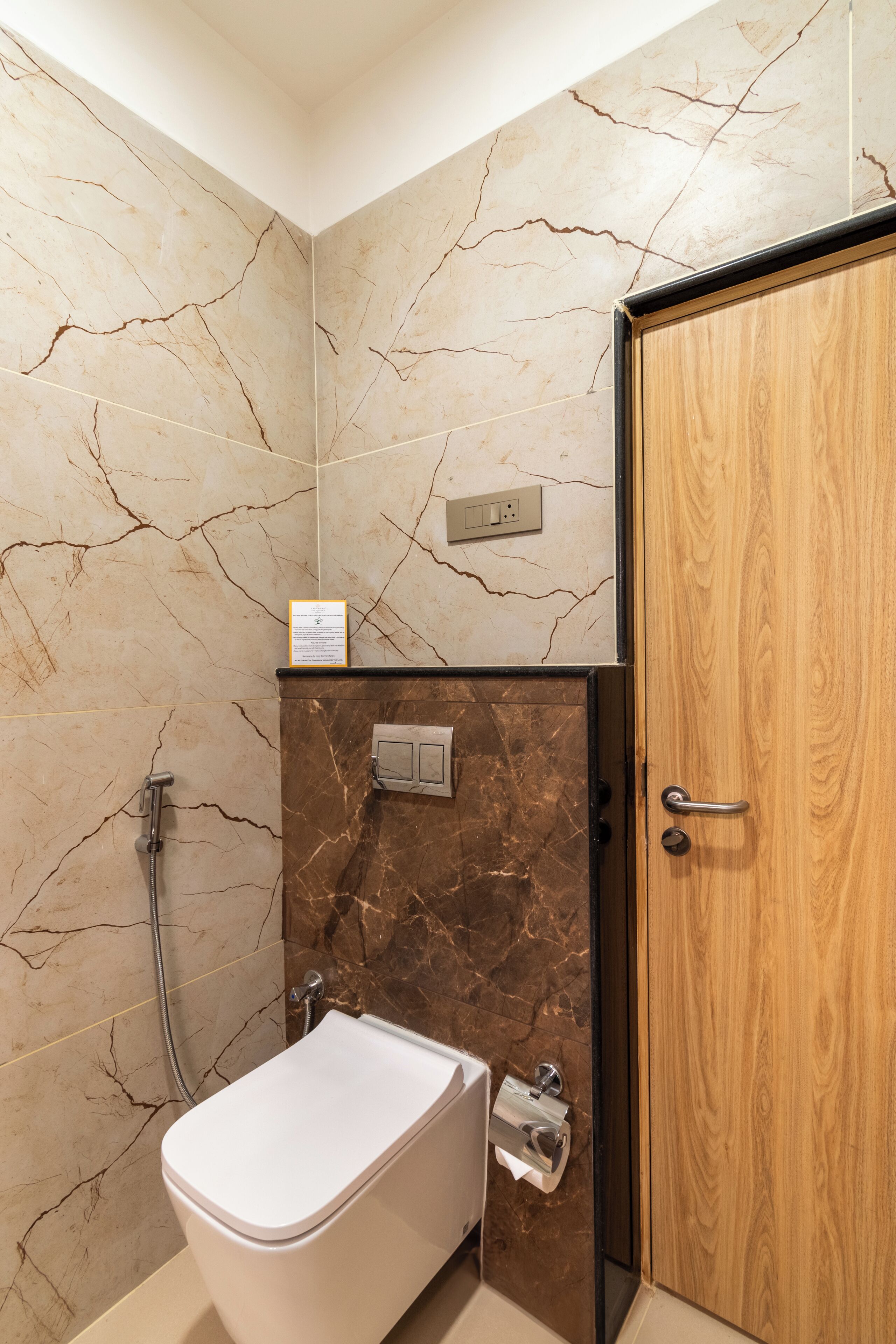 A bathroom with a marble wall, a wooden door, a shower, and a toilet.