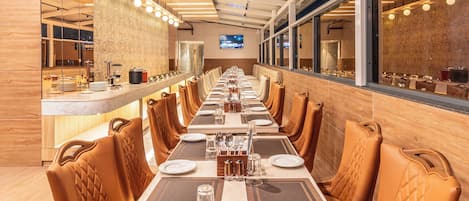 Una larga mesa de comedor con múltiples sillas, una zona de bar y una pantalla de televisión en la pared.