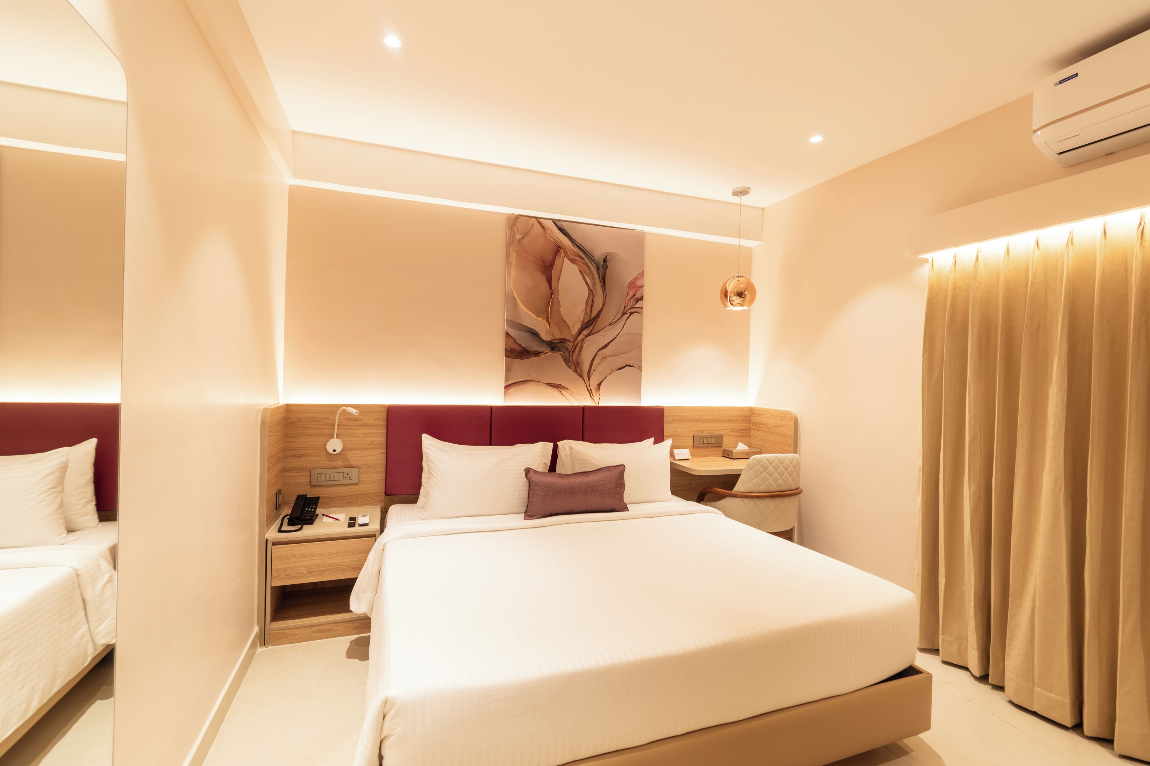 A modern hotel room with a large bed, a bedside table with a lamp, a phone, and a nightstand.