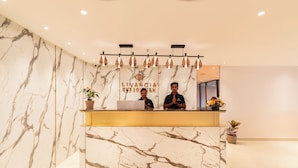 A reception desk with a marble wall backdrop, two staff members, and a laptop.