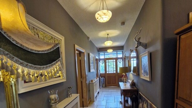 A hallway with a patterned ceiling, a radiator, a wooden cabinet, and a table with a painting. - Drumee Lodge (Castlewellan)