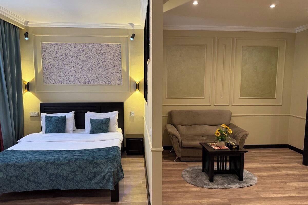 A hotel room with a bed, a sofa, a coffee table, and a wall-mounted artwork.