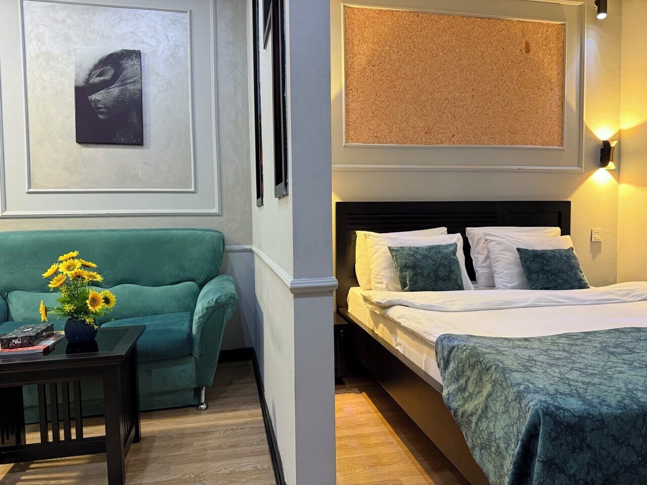 Een kamer met een groene bank, een klein tafeltje met een bloevas en een bed met een groene deken.