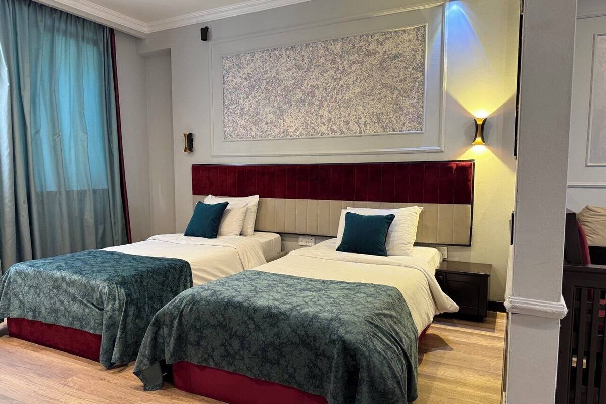 A hotel room with two beds, a large artwork on the wall, and a nightstand with a lamp.