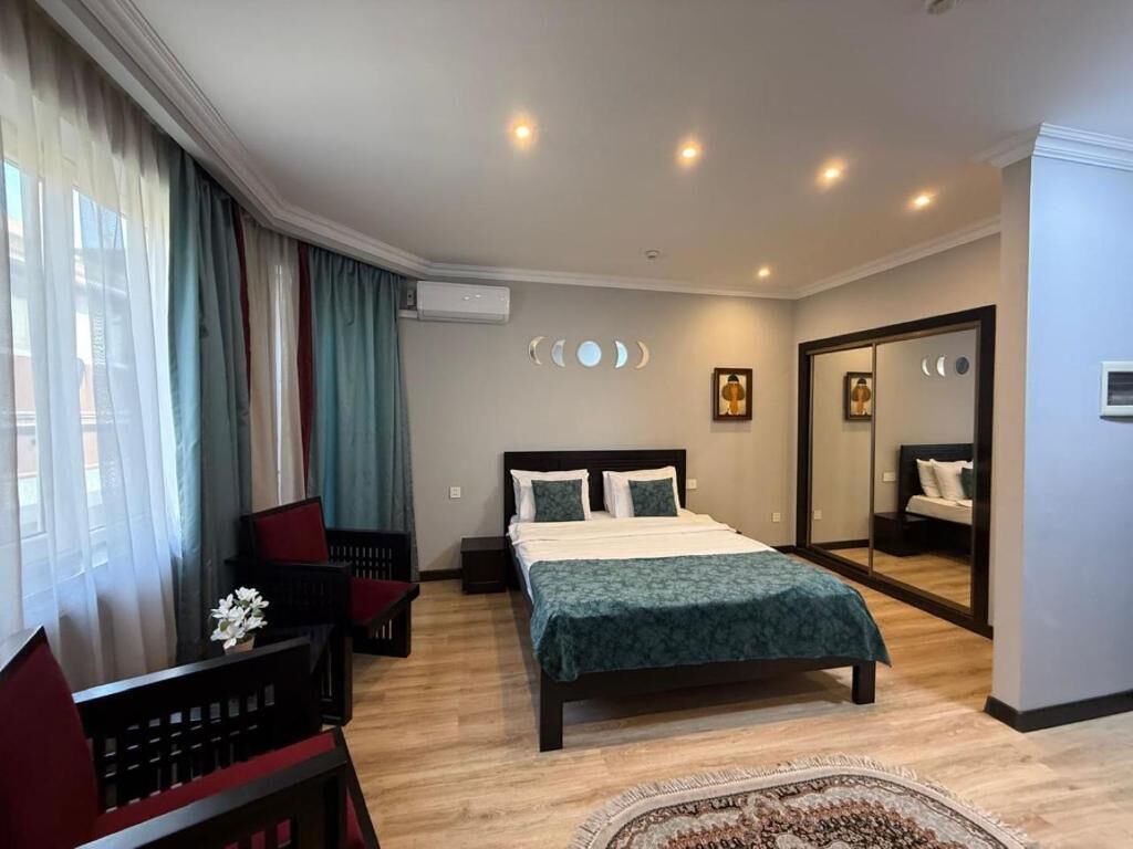 A hotel room with a bed, a desk, a chair, a mirror, and a window with curtains.