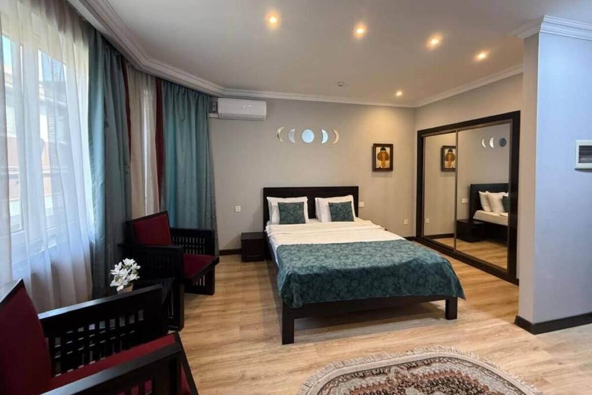 A hotel room with a bed, a desk, a chair, a mirror, and a window with curtains.