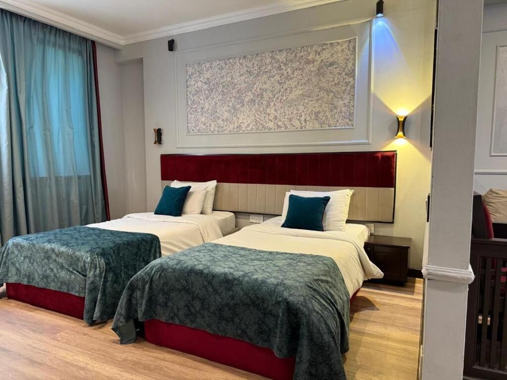 A hotel room with two beds, a red headboard, a large abstract painting, and a wall-mounted light fixture.