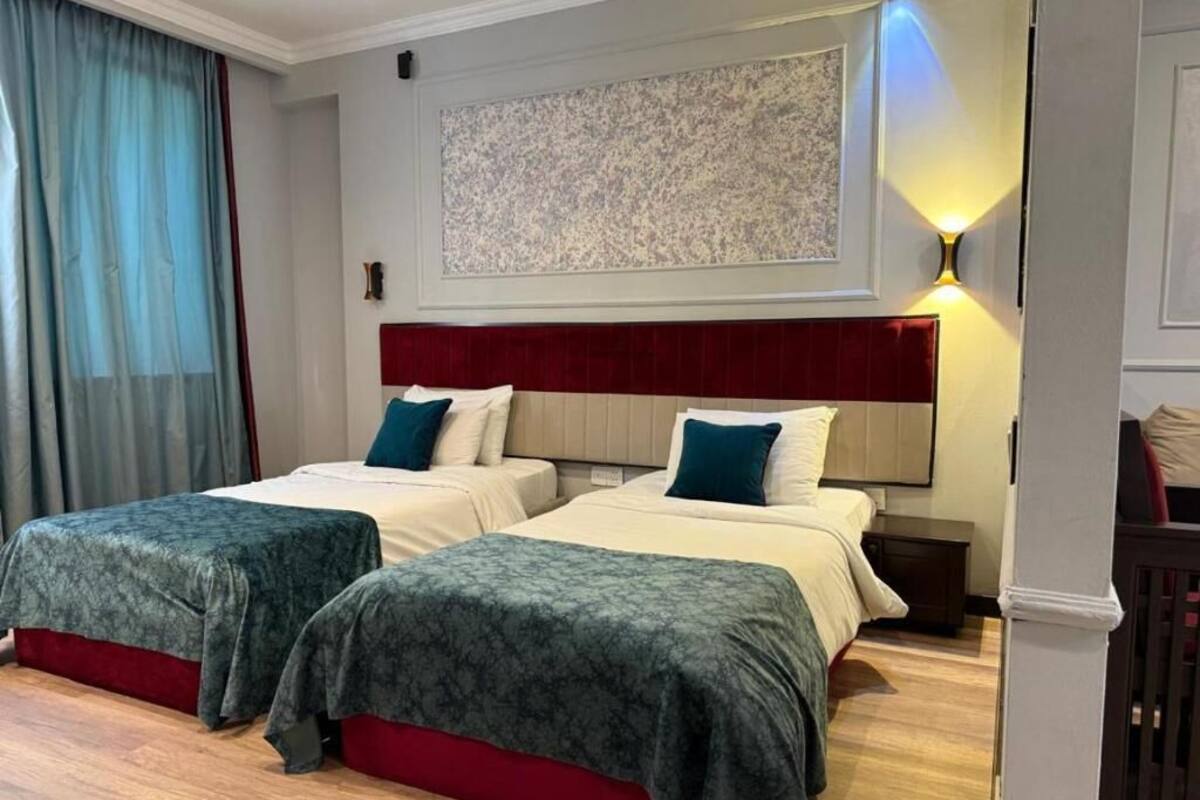 A hotel room with two beds, a red headboard, a large abstract painting, and a wall-mounted light fixture.