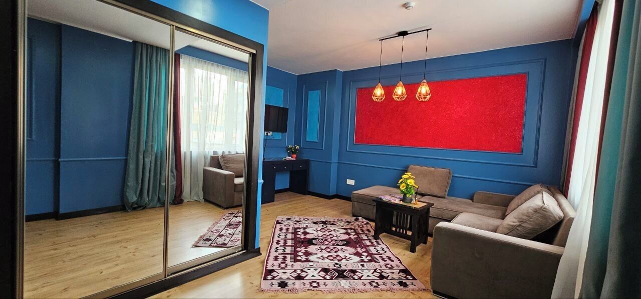 Un salon moderne avec un grand miroir, un mur d’accent rouge et un tapis à motifs.