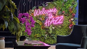 A modern interior with a neon 'Welcome to HAZZ' sign, a black armchair, and a table with books.