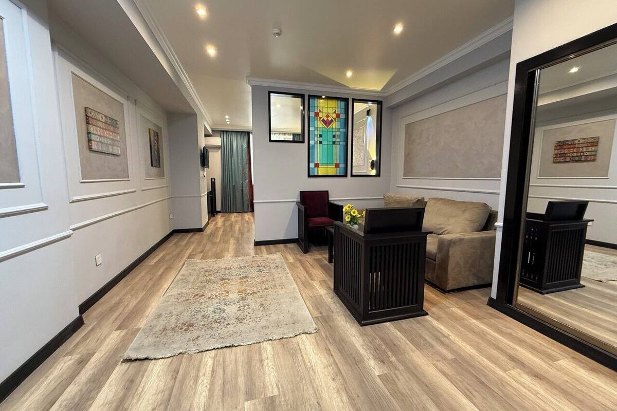 A spacious living area with a wooden floor, a large rug, a sofa, a red chair, and a black side table.