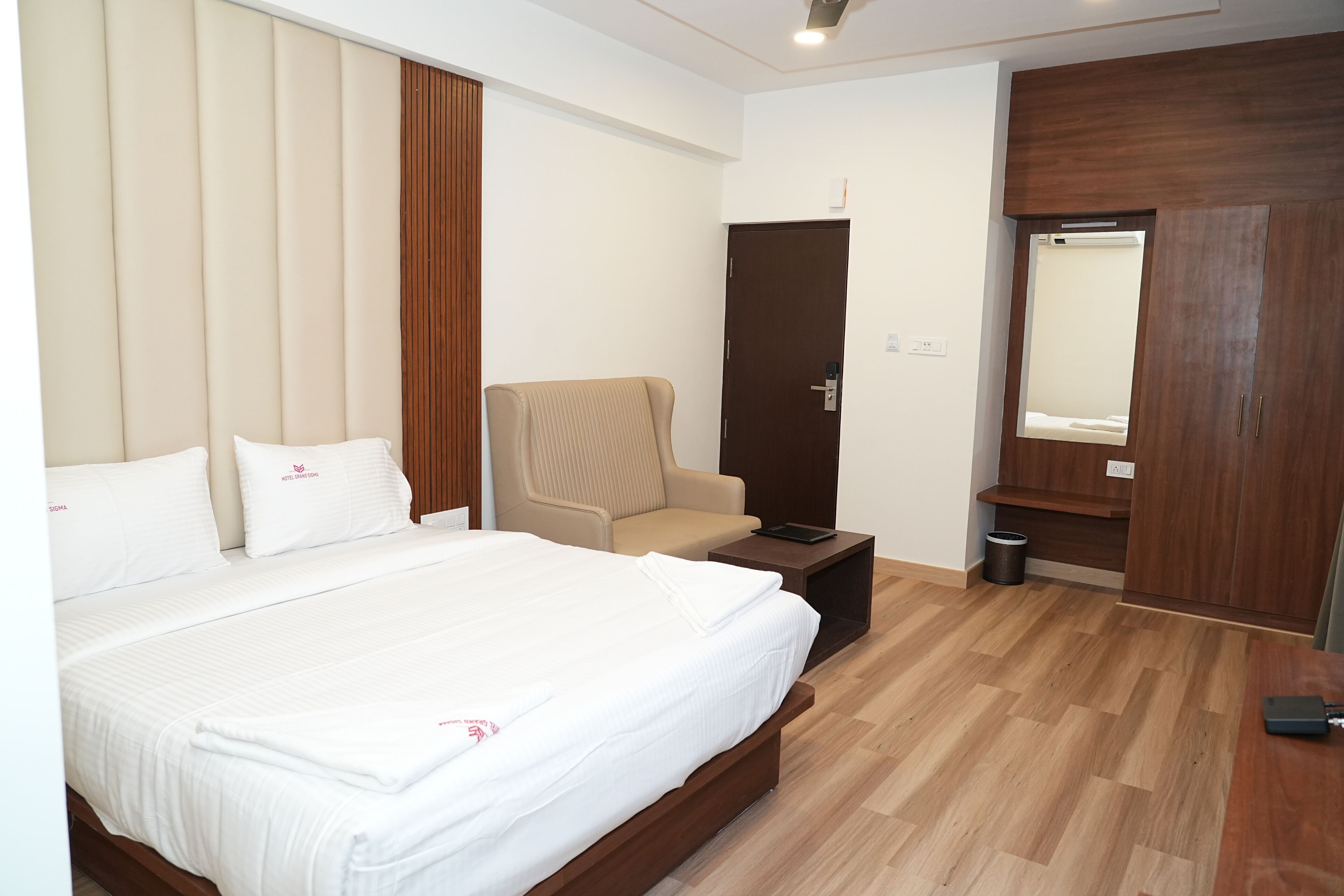 A hotel room with a large bed, a chair, a desk, and a wardrobe.