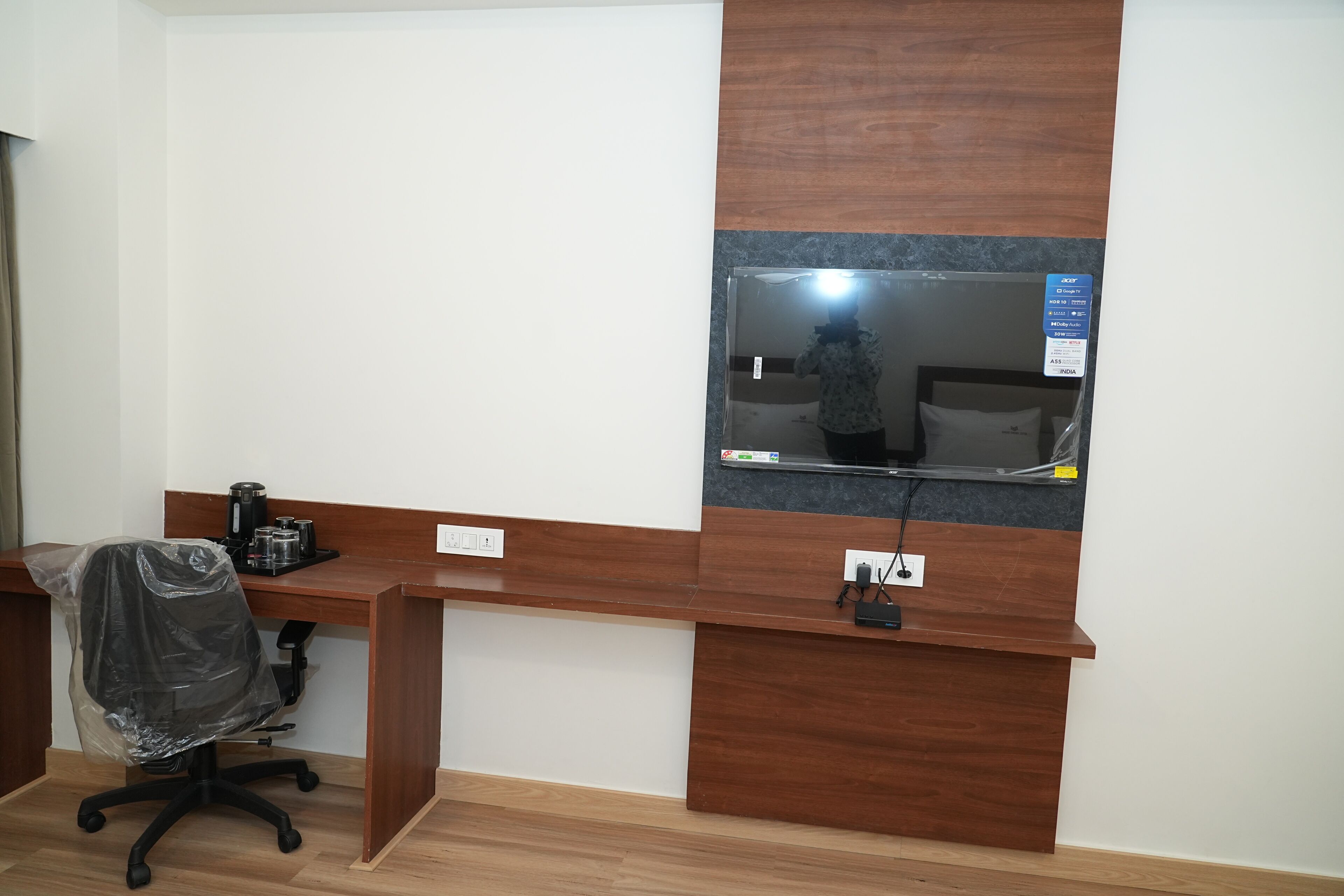 A modern office space with a wooden desk, a black office chair, a mounted flat-screen TV, and a power outlet.