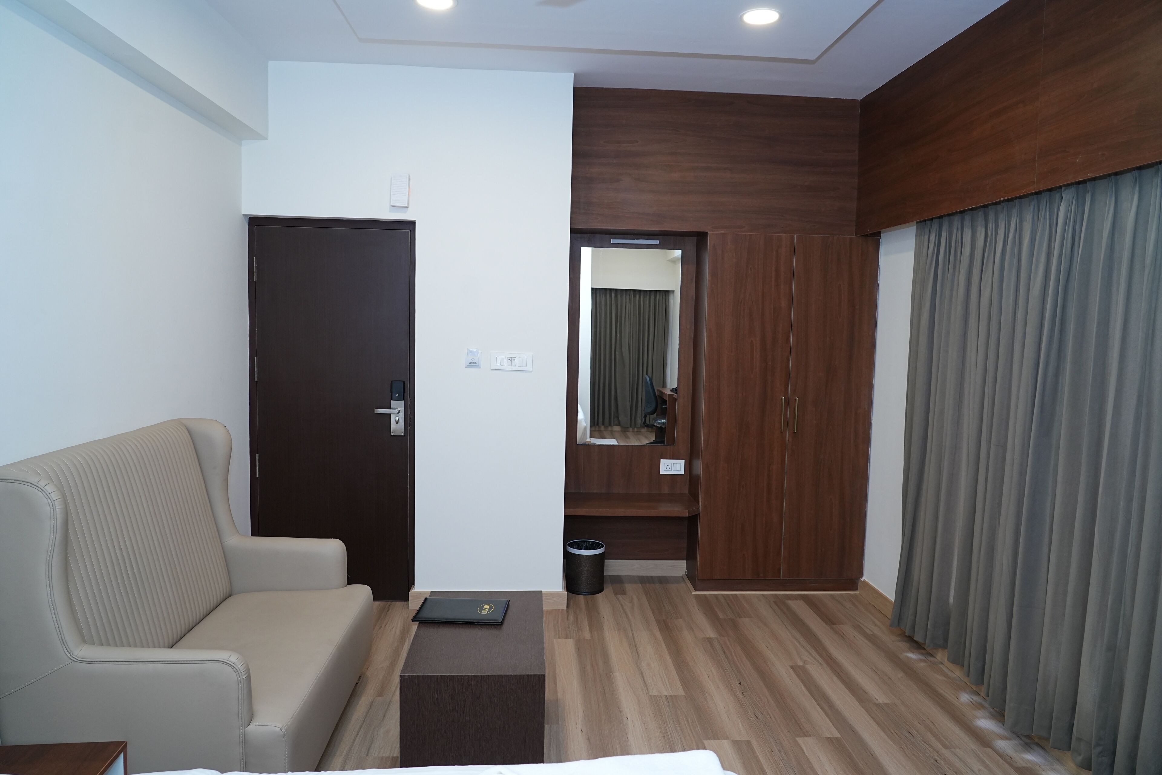 A modern hotel room with a sofa, a small table, a door, a mirror, and a curtain.