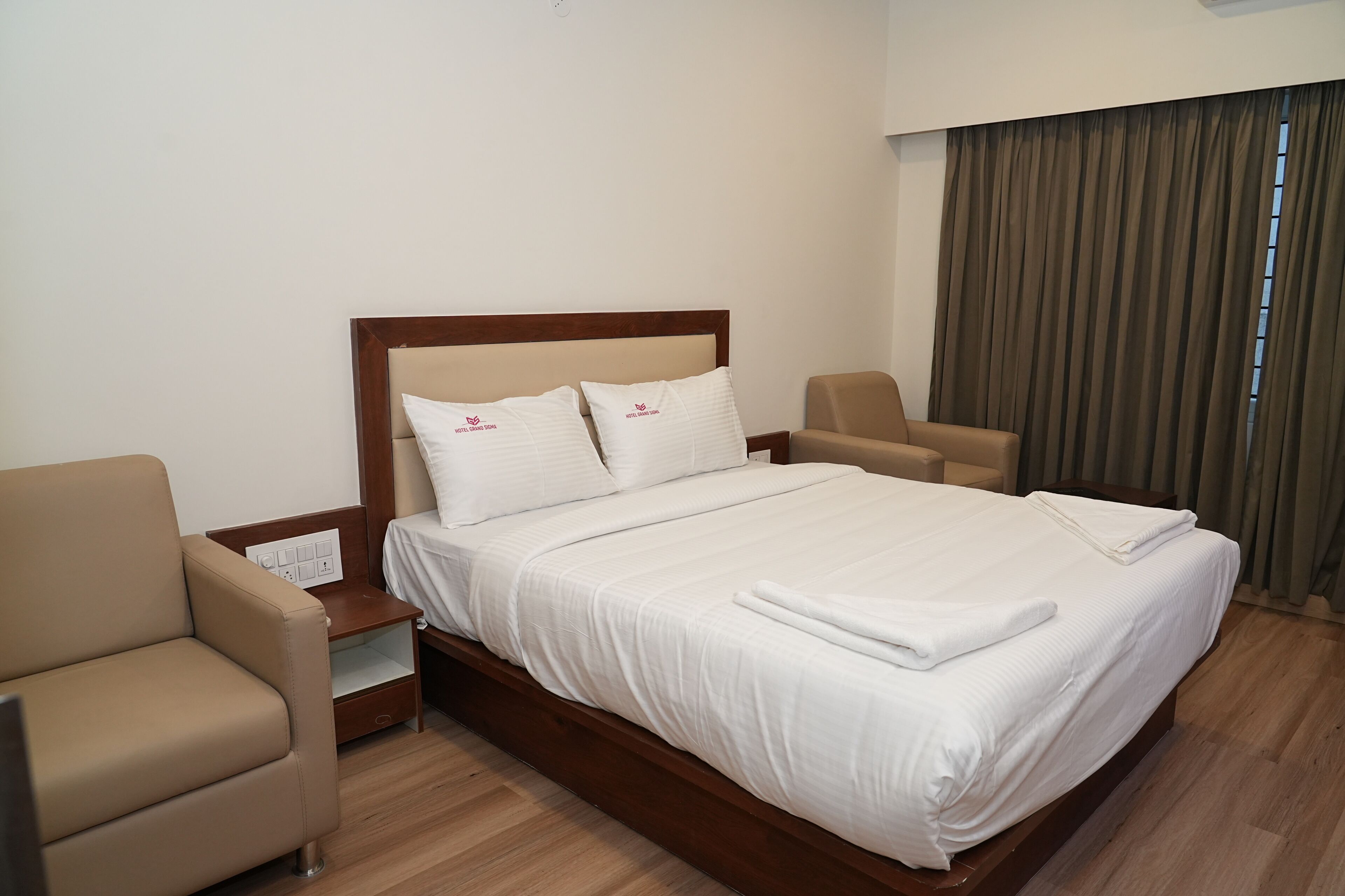 A neatly made bed with white linens and pillows, a wooden headboard, a bedside table with a lamp, and a brown armchair.