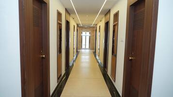 Un largo y estrecho pasillo con puertas de madera a ambos lados, que conduce a una habitación luminosa al final.