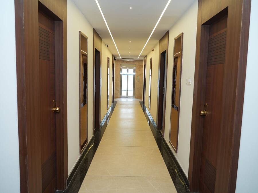 Un largo y estrecho pasillo con puertas de madera a ambos lados, que conduce a una habitación luminosa al final.