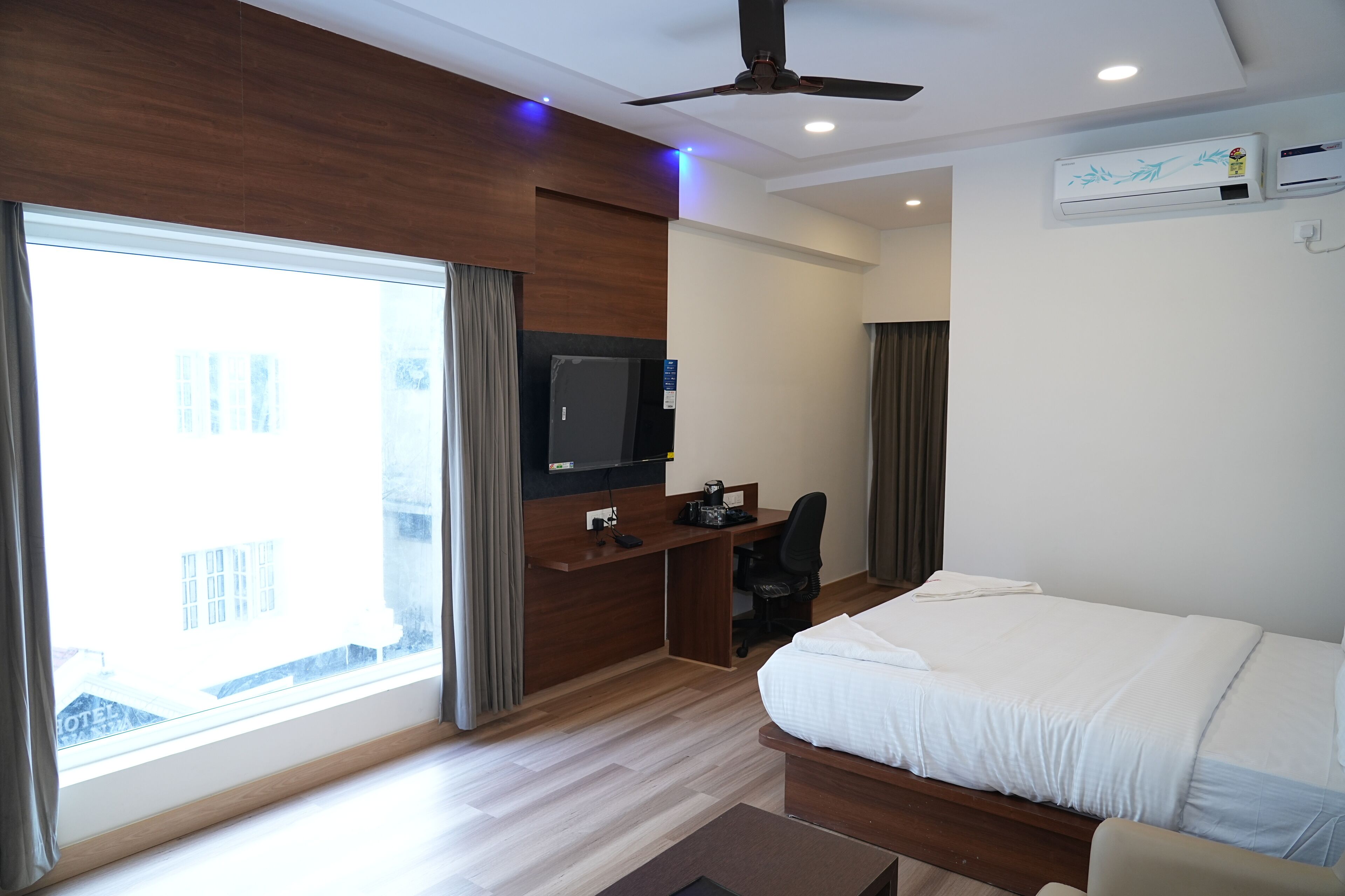Habitación de hotel con cama, escritorio, silla, televisión y ventana grande.