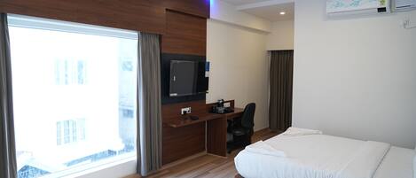 Ein Hotelzimmer mit Bett, Schreibtisch, Stuhl, Fernseher und großem Fenster.