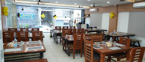 A spacious dining area with multiple wooden tables and chairs, ceiling fans, and a view of the street outside.