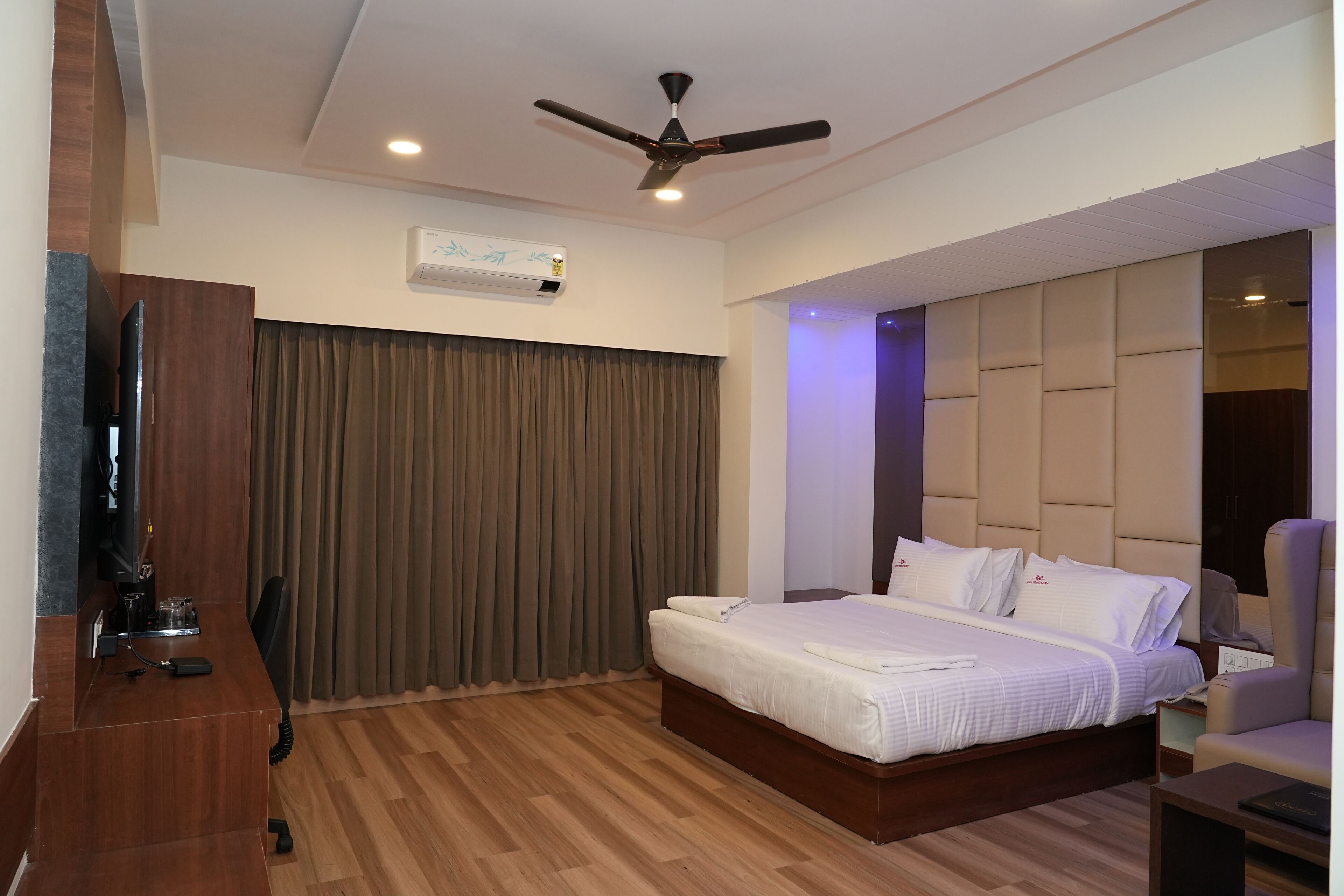 Una habitación de hotel con cama, escritorio, silla, ventilador de techo y aire acondicionado.