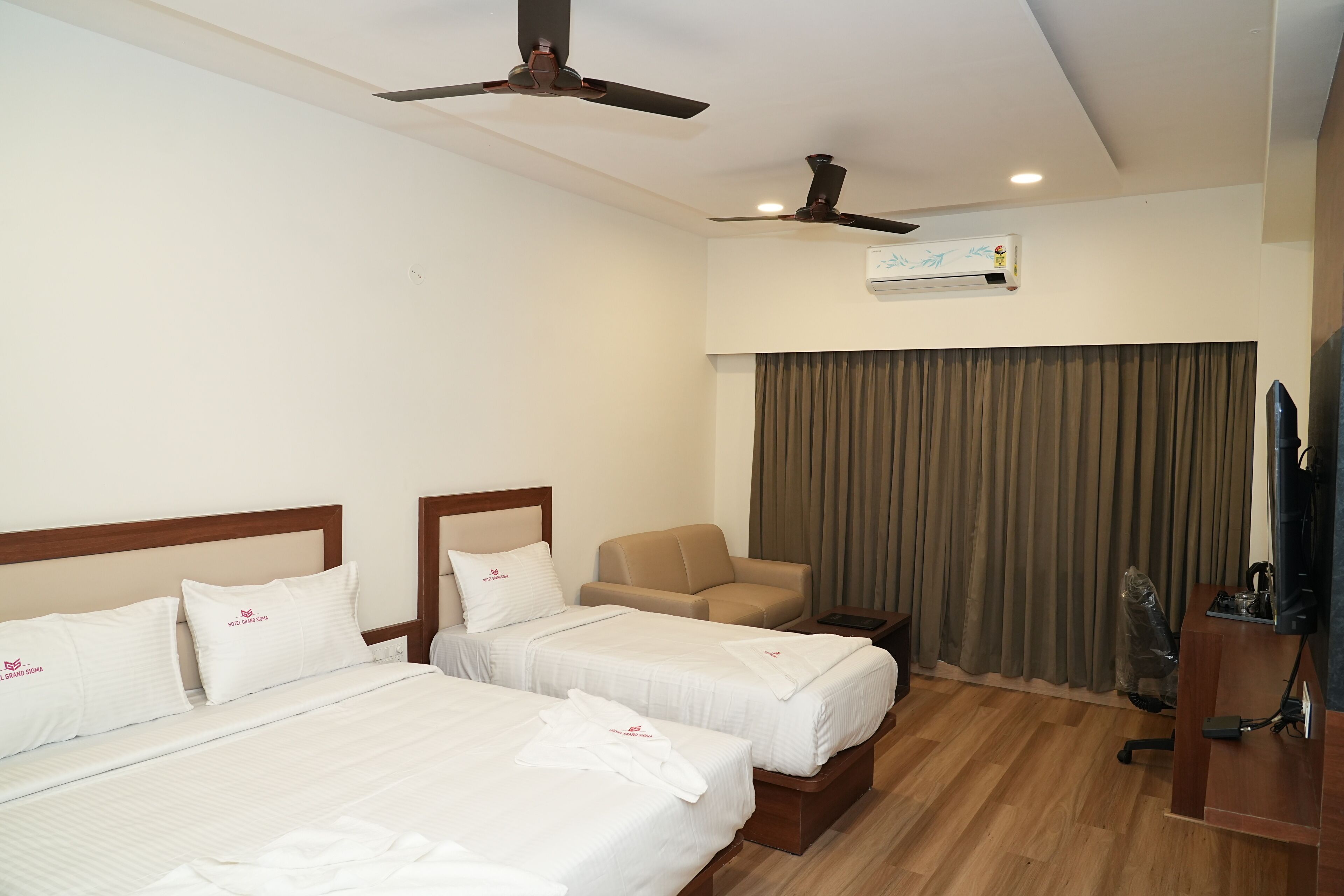 Une chambre d’hôtel avec deux lits, un canapé, une télévision et un ventilateur de plafond.