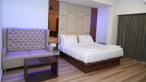 A modern hotel room with a large bed, a sofa, a small table, and a built-in headboard. - Hotel Grand Sigma (Bengaluru)