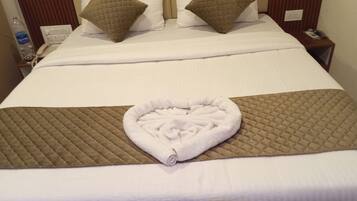Una cama bien hecha con una toalla con forma de corazón y dos almohadas, una botella de agua y un teléfono en la mesita de noche.