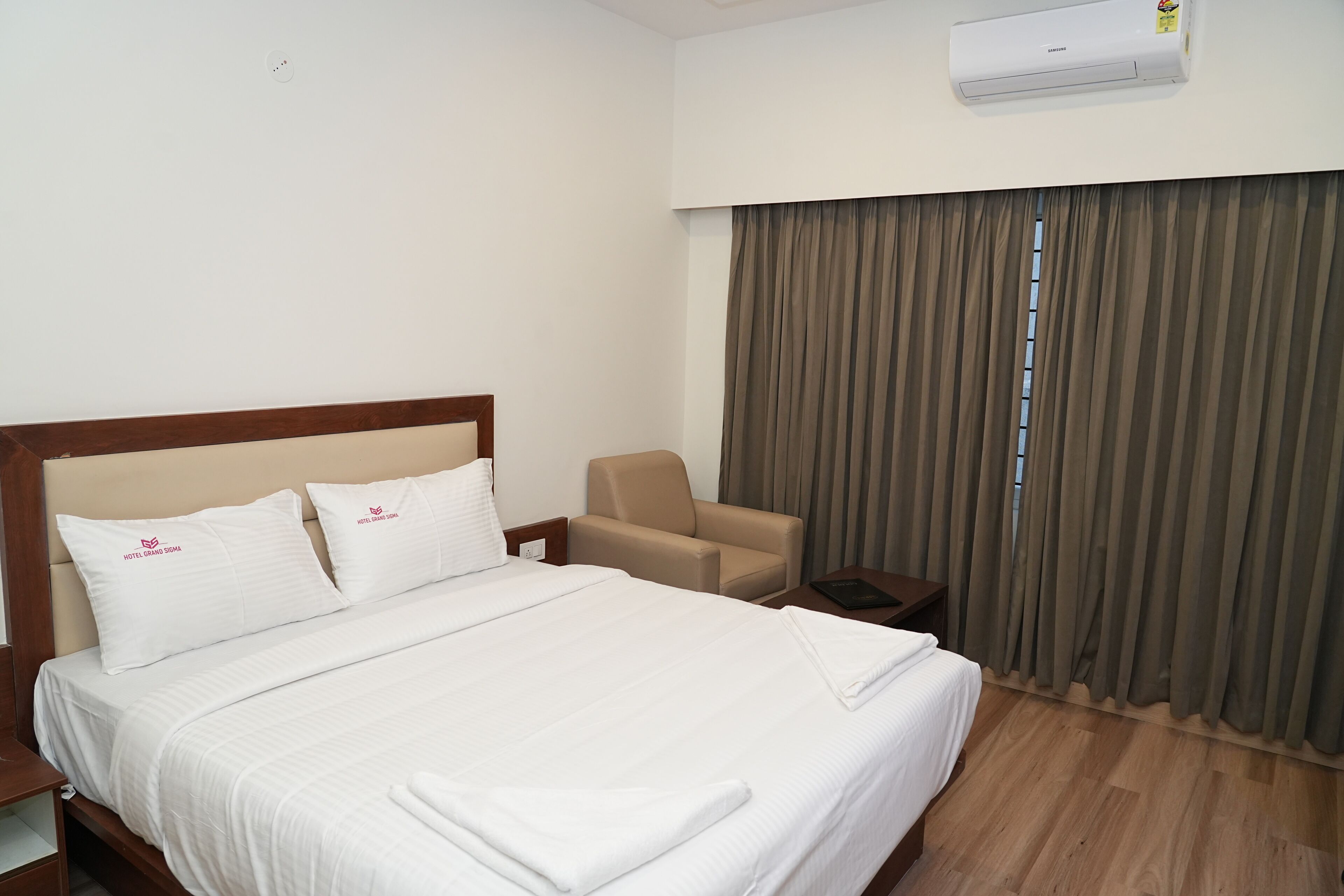 A hotel room with a large bed, a chair, a nightstand, and a window with curtains.