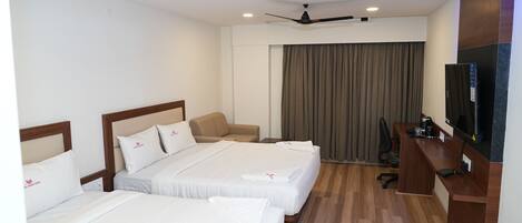 A hotel room with three beds, a desk, a television, and ceiling fans.