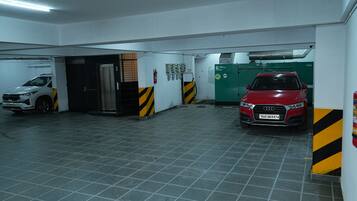 A parking garage with two cars, a white SUV and a red car, and a fire extinguisher on the wall.