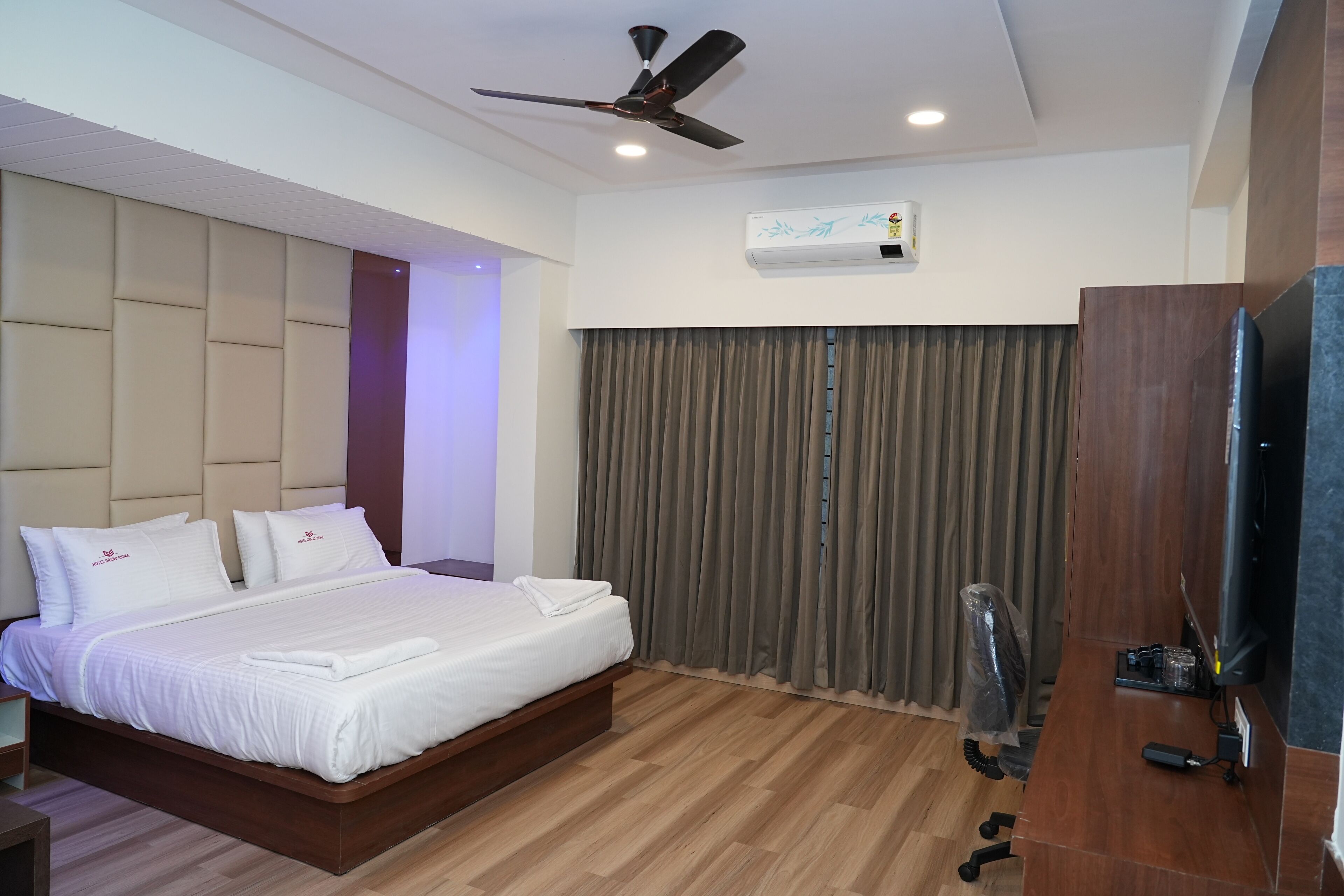 Une chambre d’hôtel moderne dotée d’un grand lit, d’un ventilateur de plafond, d’un climatiseur, d’un bureau avec un ordinateur et d’une télévision.