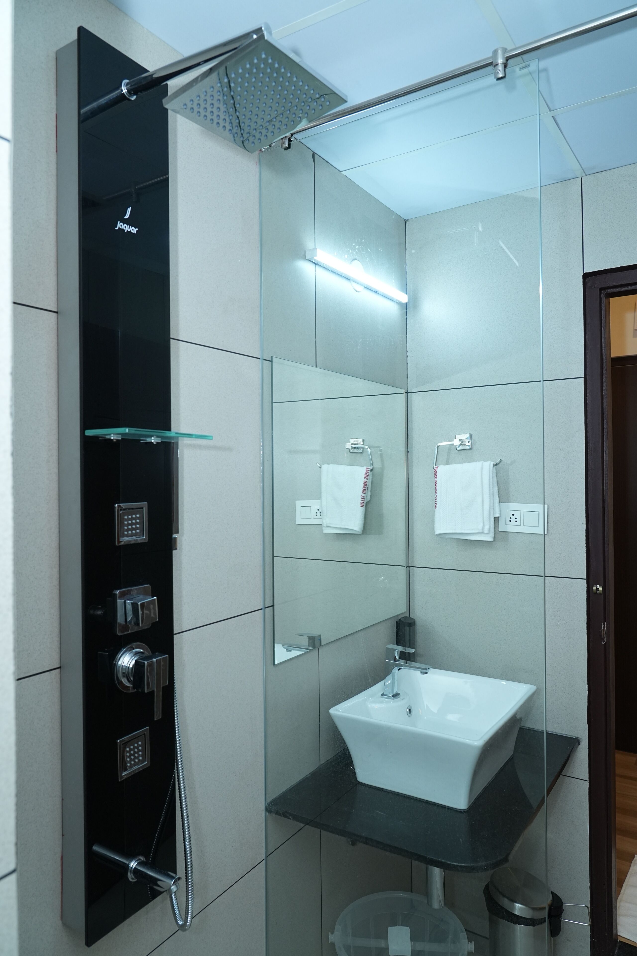 A modern bathroom with a glass-enclosed shower, a white sink, and two white towels on towel hooks.