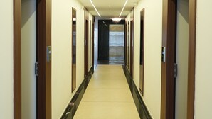 A long, narrow hallway with wooden doors on both sides, a tiled floor, and a ceiling with recessed lighting. - Hotel Grand Sigma (Bengaluru)